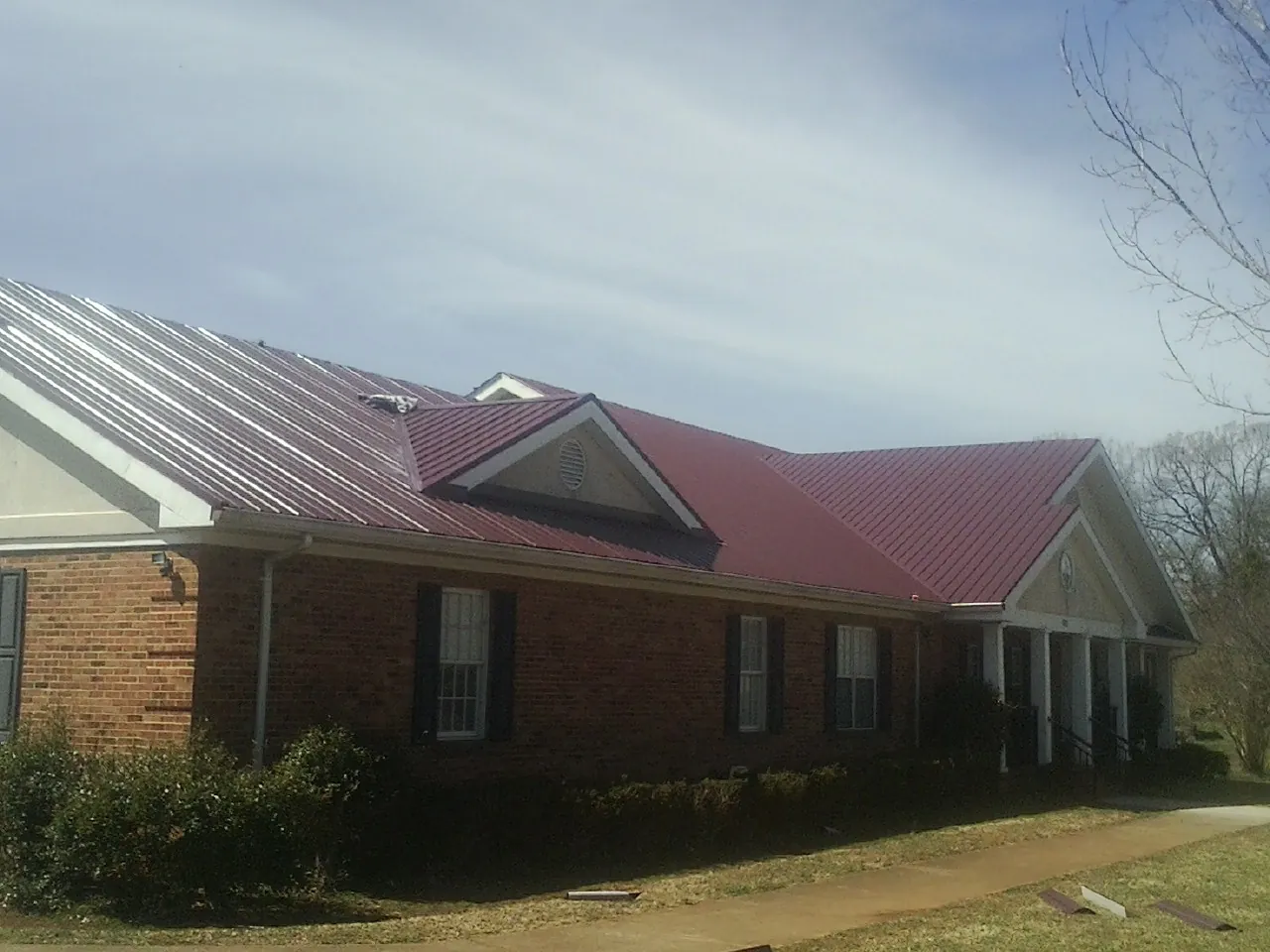 Red metal roof with gabled entries on a long brick building, from a Hail Damage Roof Repair job in Dawson