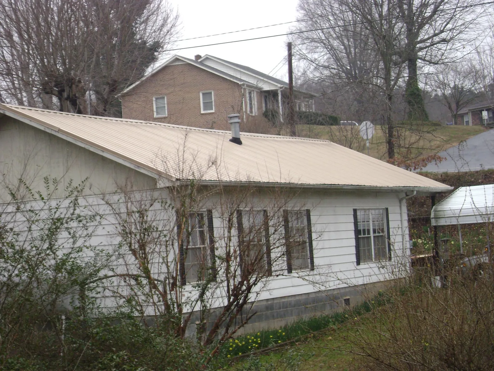 Tan metal roof on a white sided house set into a hillside — Commercial Roofing by Roofing Brothers in Dawson